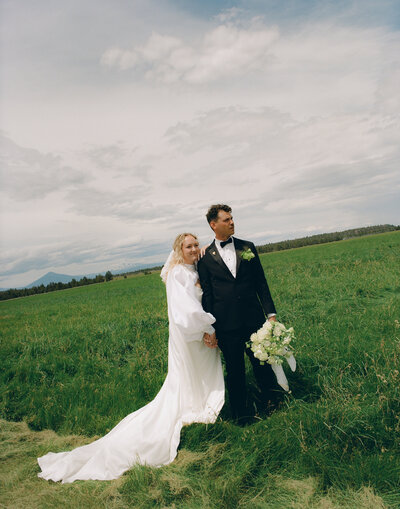 Bride and groom standing in an open field under dramatic skies | Summer luxury wedding in Bend Oregon captured on film by Tess Gearhart