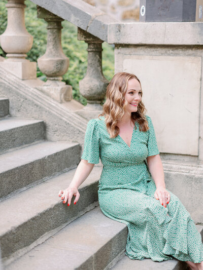 a woman in a green dress sitting on some steps looking away and smiling