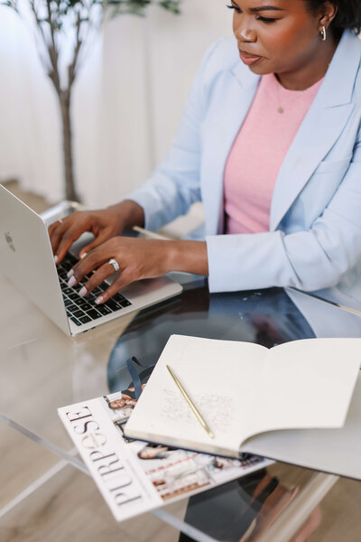 Black career coach for working women typing at computer on glass table with notebook open