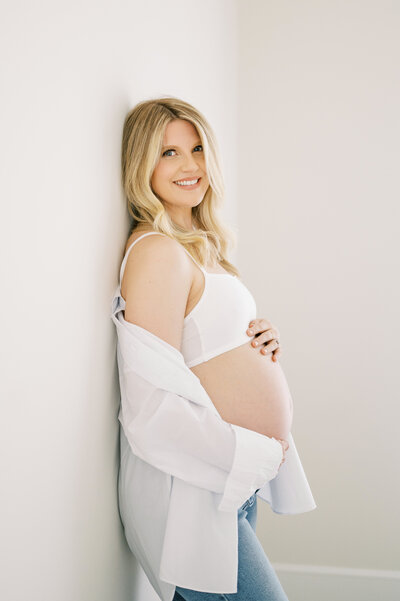 Expecting mom holds bare pregnany belly and smiles at the camera during a studio maternity session at the Worth Capturing Studio in Raleigh North Carolina.