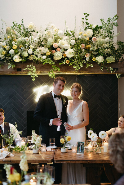 A couple smiles as they gaze over their wedding reception during dinner in Prince Edward County