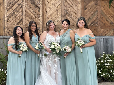 Bride and bridesmaids in sage green dresses holding white bouquets