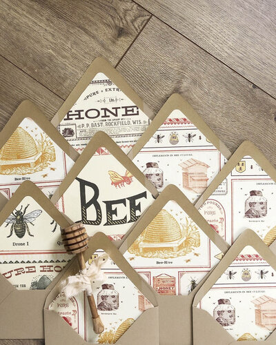 Kraft envelopes laying against a wood floor, featuring envelope liners with vintage-style honey and bee illustrations
