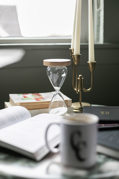 Ashleigh C. Henry, life coach and author, set up a vignette of a gold candela with a coffee cup and an hour glass, near a dark green paneled wall.