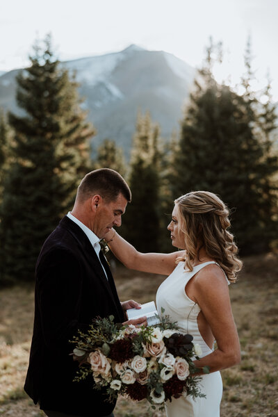 Bride touches groom's face during emotional vow exchange in forest near Breckenridge, Colorado.