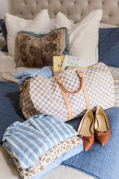 Louis Vuitton weekender duffel sits on bed with clothing ready for packing