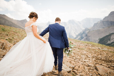 This stunning photograph captures the bride and groom walking down a mountain hand in hand after their helicopter adventure elopement. Surrounded by towering peaks, the dramatic landscape emphasizes the beauty and adventure of their special day.
