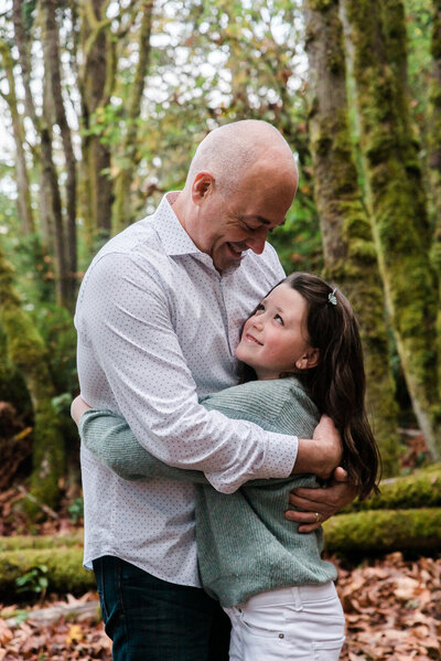 Father hugging his daughter at outdoor fall family photos with forest in background