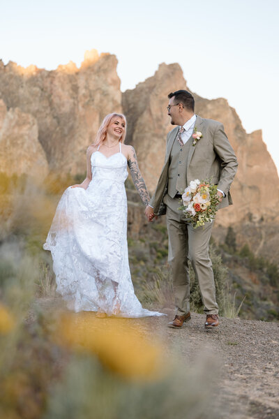 Bride and groom walking at Smith Rock State Park. There are yellow flowers in the foreground.