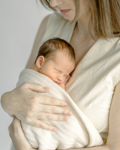 Fine-art newborn photography session in Miami featuring mom holding baby with natural tones