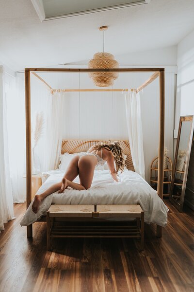 A blonde woman in a Denver boudoir studio wearing white lingerie and crawling on a bed