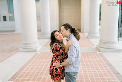 Groom to be kisses his Bride's cheek amongst the pillars at LA City Hall