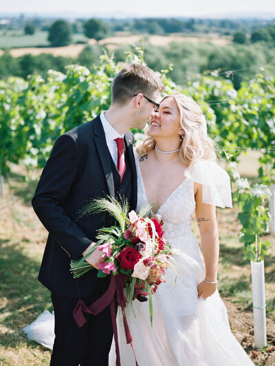 bride and groom looking at each other and smiling in between vines at hencote vineyard 