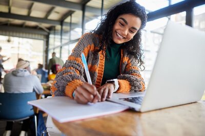 Girl in a green shirt and orange and grey sweater smiling as she studies for her PA exams