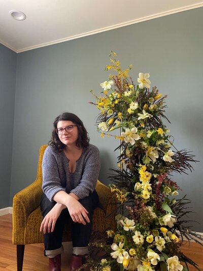 Jillian Santora sitting in front of yellow themed floral display. Owner of Jessamine Floral and Events, in New Jersey & Philadelphia
