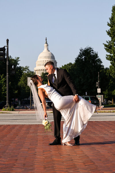 A groom dipping a bride outside in front of a government building.