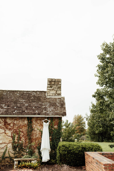 Wedding dress hanging outside on an ivy-covered building.