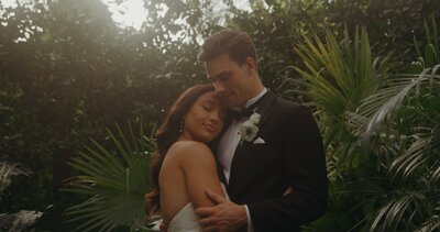bride and groom embrace in front of foliage