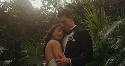 bride and groom embrace in front of foliage