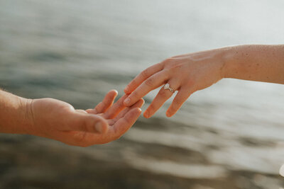 Close-up of a couple’s hands showing off an engagement ring over water during their NYC engagement session, captured by New York City wedding and elopement photographer Dom Augustine.