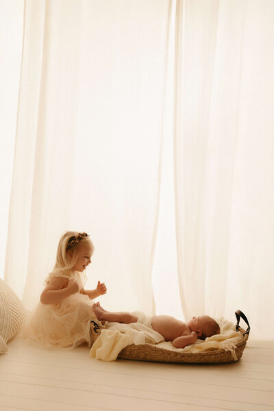 Older sibling gently cuddling newborn baby during cozy studio photo session in Nashville