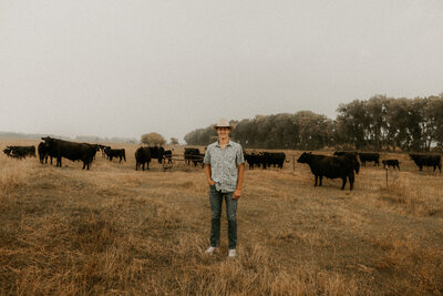 Photo of a senior boy standing in a cattle pasture posing with his cows.