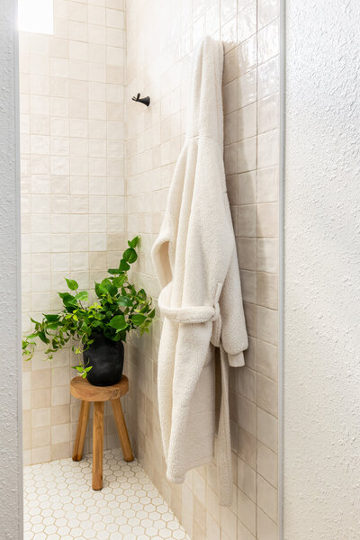Decorative stool with faux plants and robe hanging inside entry area of a fully custom walk-in tile shower