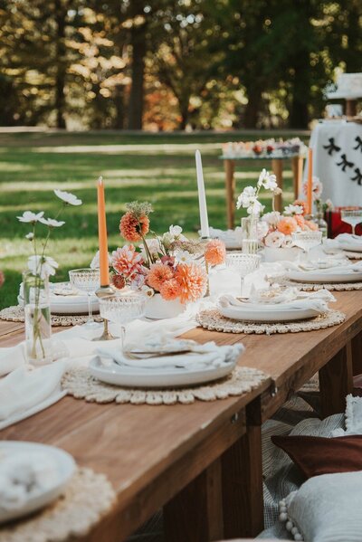 Wooden picnic table styled with orange and white florals, taper candles, and elegant place settings, designed by Yours Truly, a wedding planner and designer in New Jersey.