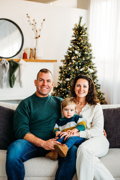 Smiling family sitting by a decorated Christmas tree during Ottawa holiday mini session.