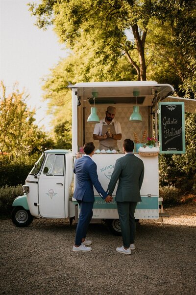 Two grooms holding hands and ordering from a gelato truck during their wedding in Tuscany, Italy!