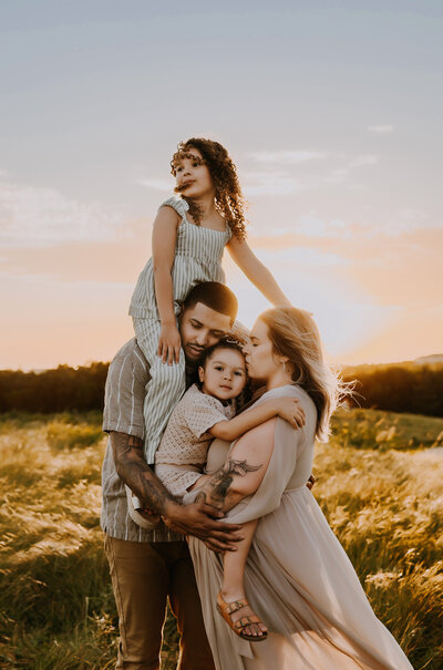 a family of four standing in the middle of a long, grassy field cuddling and hugging each other at Arbor Hills Nature Preserve in Plano, texas