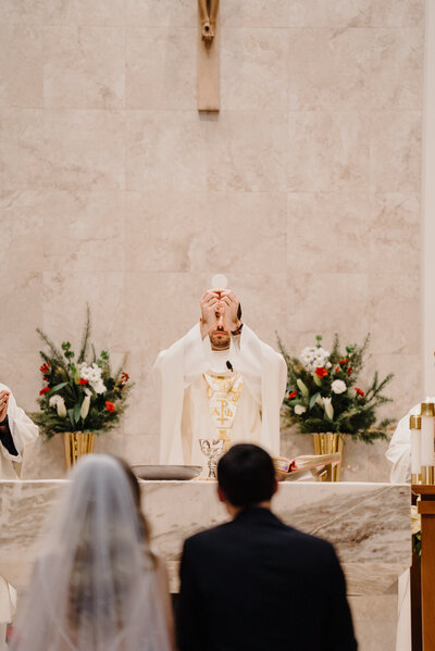 Bride and groom kneel at the altar in a beautiful, bright Catholic Church wedding, decorated for Christmas. Photo taken by Orlando Wedding Photographer Four Loves Photo and Film.
