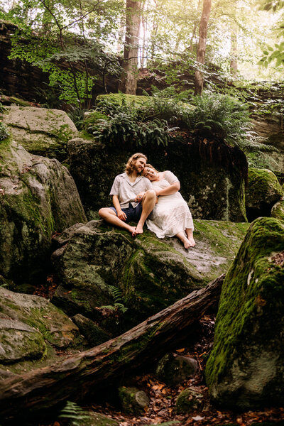 Couple snuggles close amongst large mossy boulders 