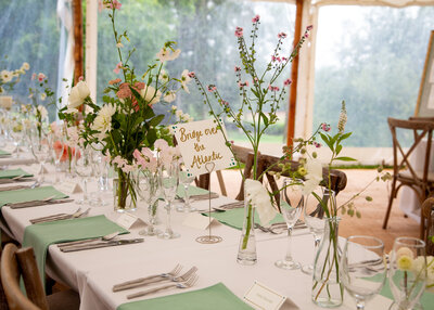 Bud vases of flowers on the tables in a marquee, with green napkins