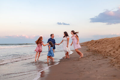 A joyful family runs barefoot along the shoreline at sunset, laughter echoing as the waves dance beside them in a golden Virginia Beach glow. 