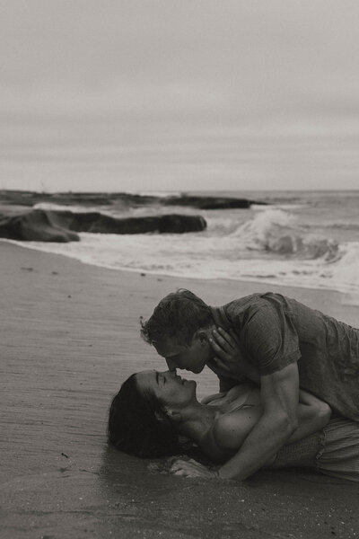 steamy engagement session, beach session, couple on sand with water 