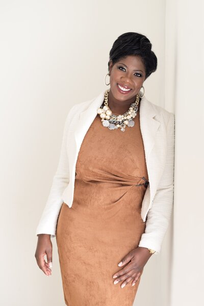 wedding designer in gold dress and cream blazer smiling at camera