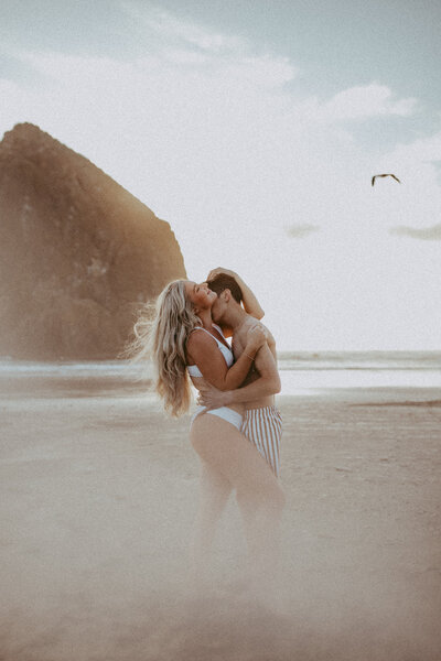 A couple in swimsuits loving on each other while the seaguls fly overhead at Cannon Beach in Oregon. 