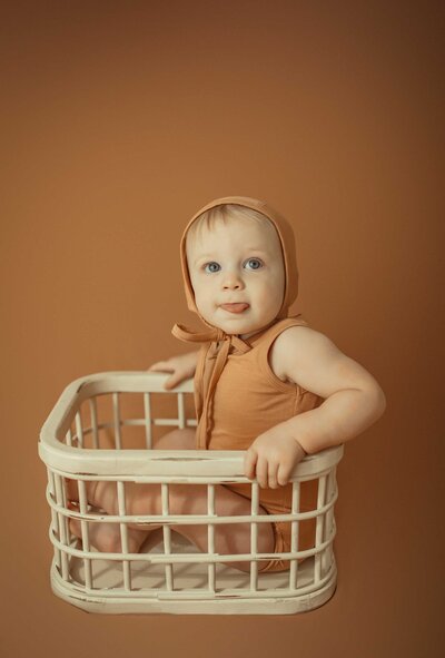 Capturing innocence with the best photographer in the area in a simple yet charming photo session. The adorable blond baby boy, dressed in a delightful brown outfit, is the star of the scene as he rests inside a wooden cradle.