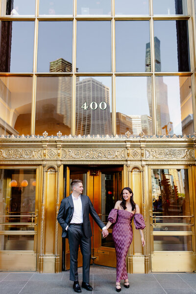 Engaged couple takes engagement photos outside the Wrigley Building in Chicago