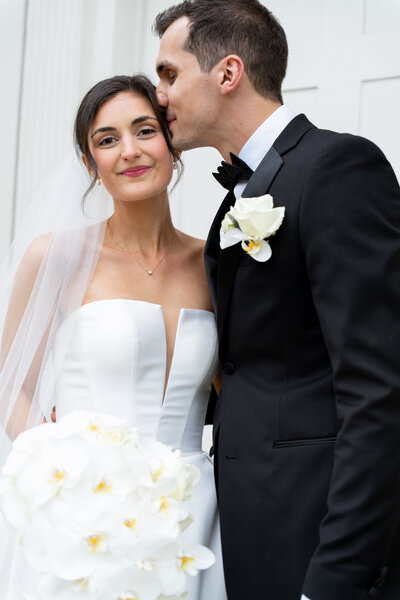 Groom kissing bride on temple as they pose for portraits after they got married. 
