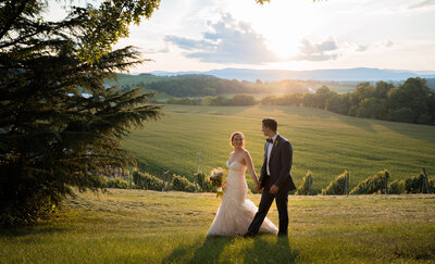 The bride and groom are walking with the sun and mountains behind them with a sun flare. This photo was taken by Mason Jesmer.