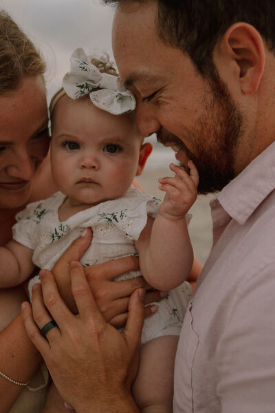 Close-up of a baby girl with a bow, held by her smiling parents at the beach