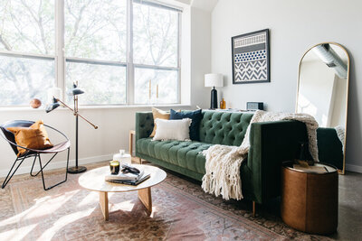White living room with green velvet tufted sofa, vintage rug, cane and wood coffee table and leather chair and side table