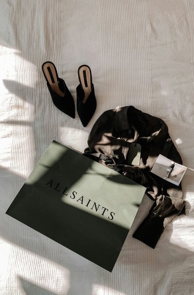 A green AllSaints shopping bag laying next to a black top and black heels