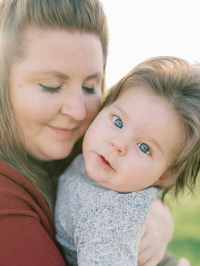 Mother holding one year old son with eyes softly closed while son with long hair looks directly at the view by Portland Family Photographer Emilie Phillipson Photography.