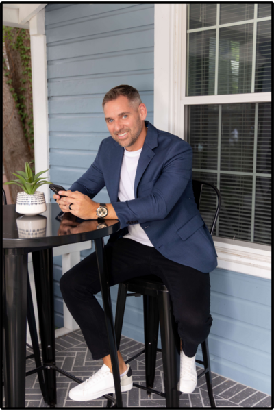 photo of a man sitting at a table with phone in hand smiling at the camera