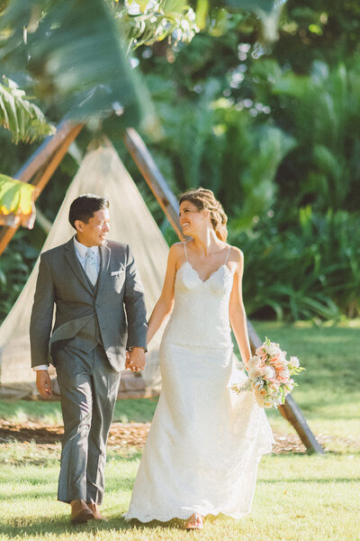 couple walking hand in hand. Bride has a bouquet and groom is wearing a grey suit