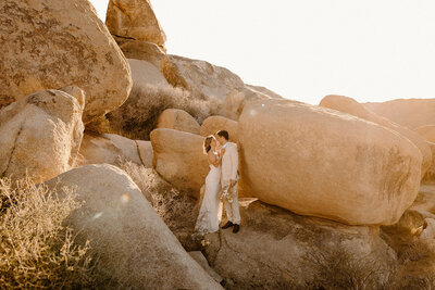 Bride and groom standing between massive desert boulders in Joshua Tree, sharing a quiet moment during their adventurous elopement.