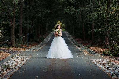 solo bride wearing a Kiera Elise Bridal dress holding a bouguet while  standing on a dark roadway in a spot of light at Grey Towers National Historic Site in Milford, Pennsylvania